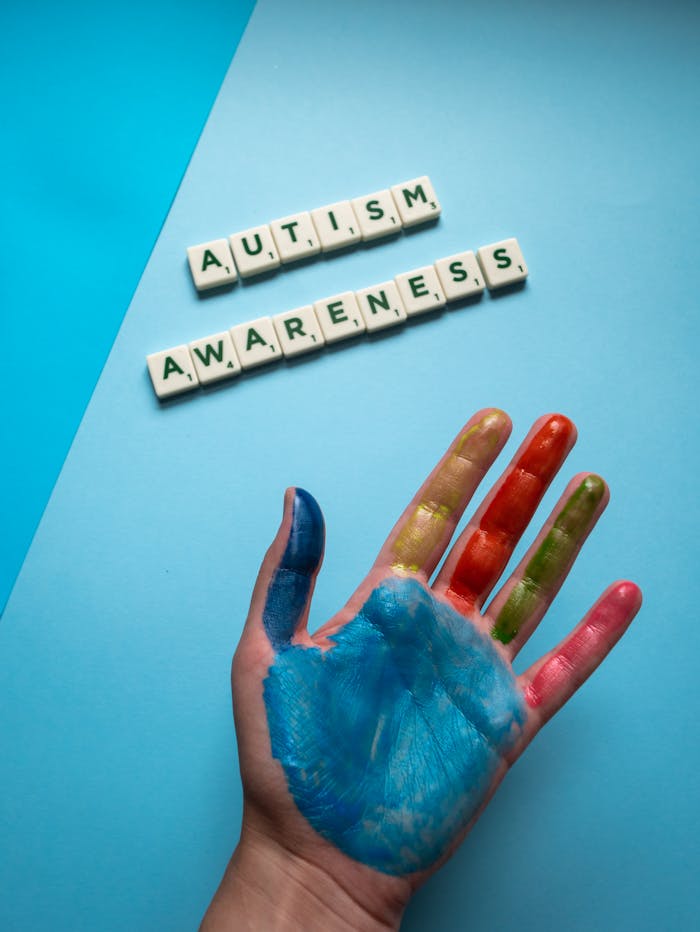 Crafting Captivating Headlines: Your awesome post title goes here A top view of a colorful painted hand next to autism awareness scrabble tiles on a blue background.